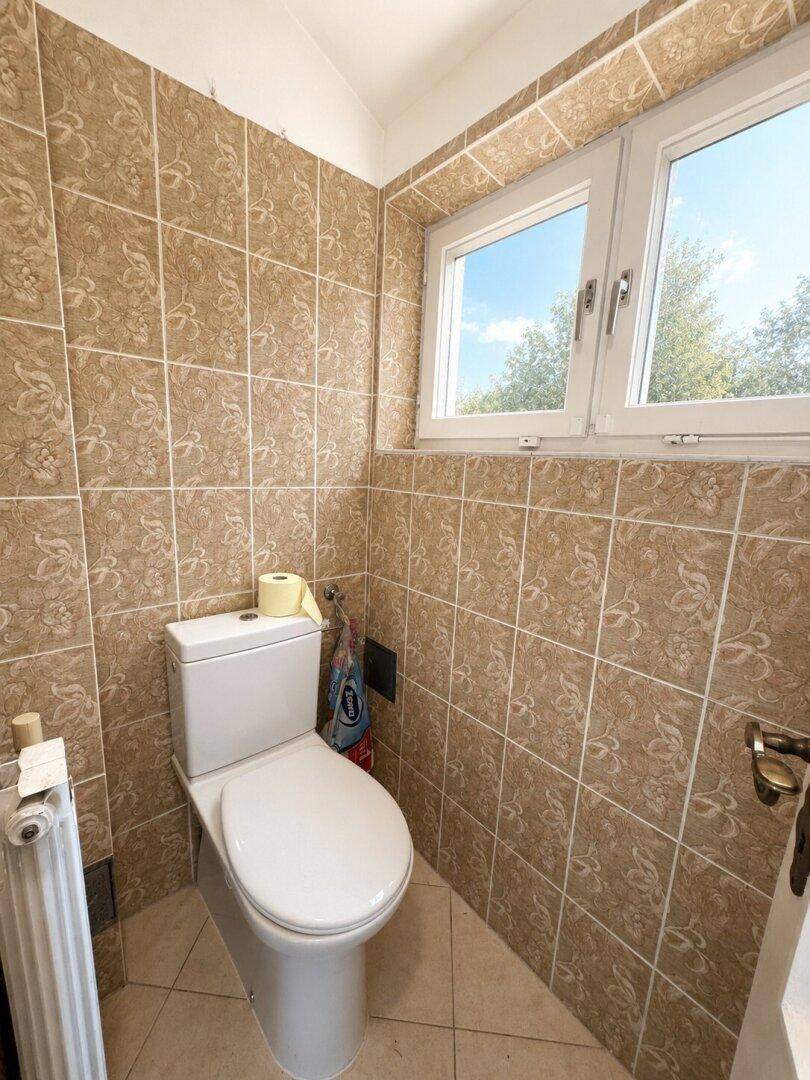 Separate Toilette mit Fenster und beigefarbenen Fliesen an den Wänden.