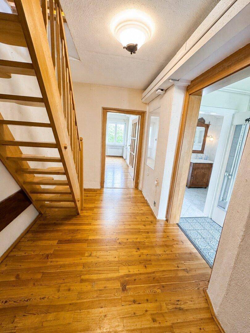 Heller Flur mit Holztreppe und Zugang zu weiteren Räumen, inklusive Badezimmer.