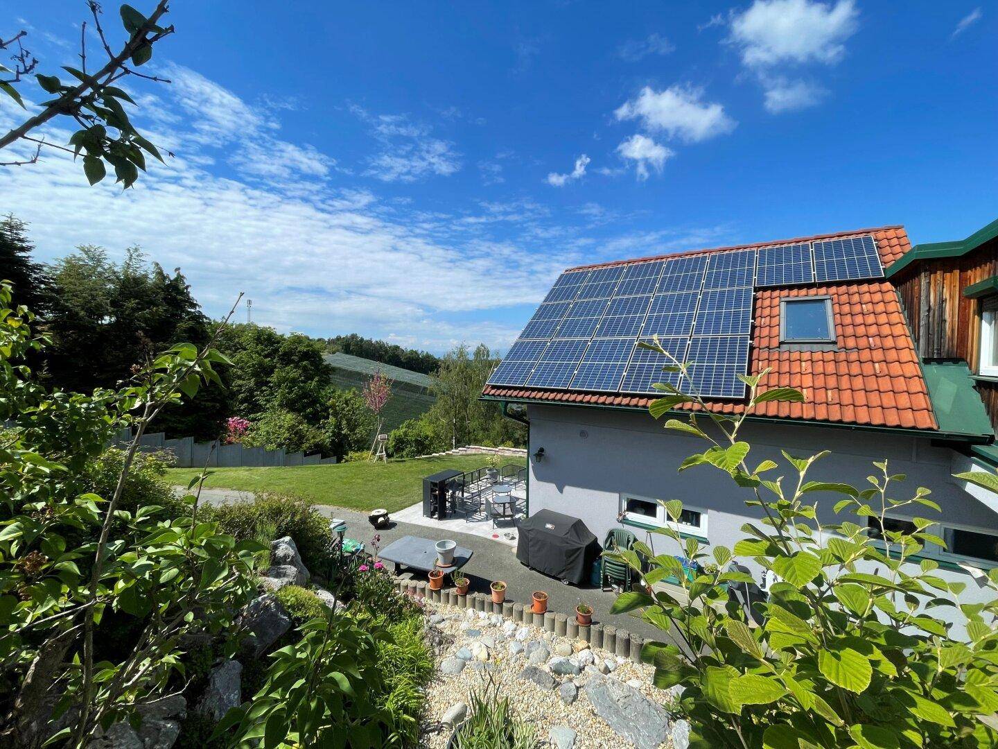 Blick vom Garten auf das Haus mit Solaranlage und die malerische grüne Hügellandschaft.