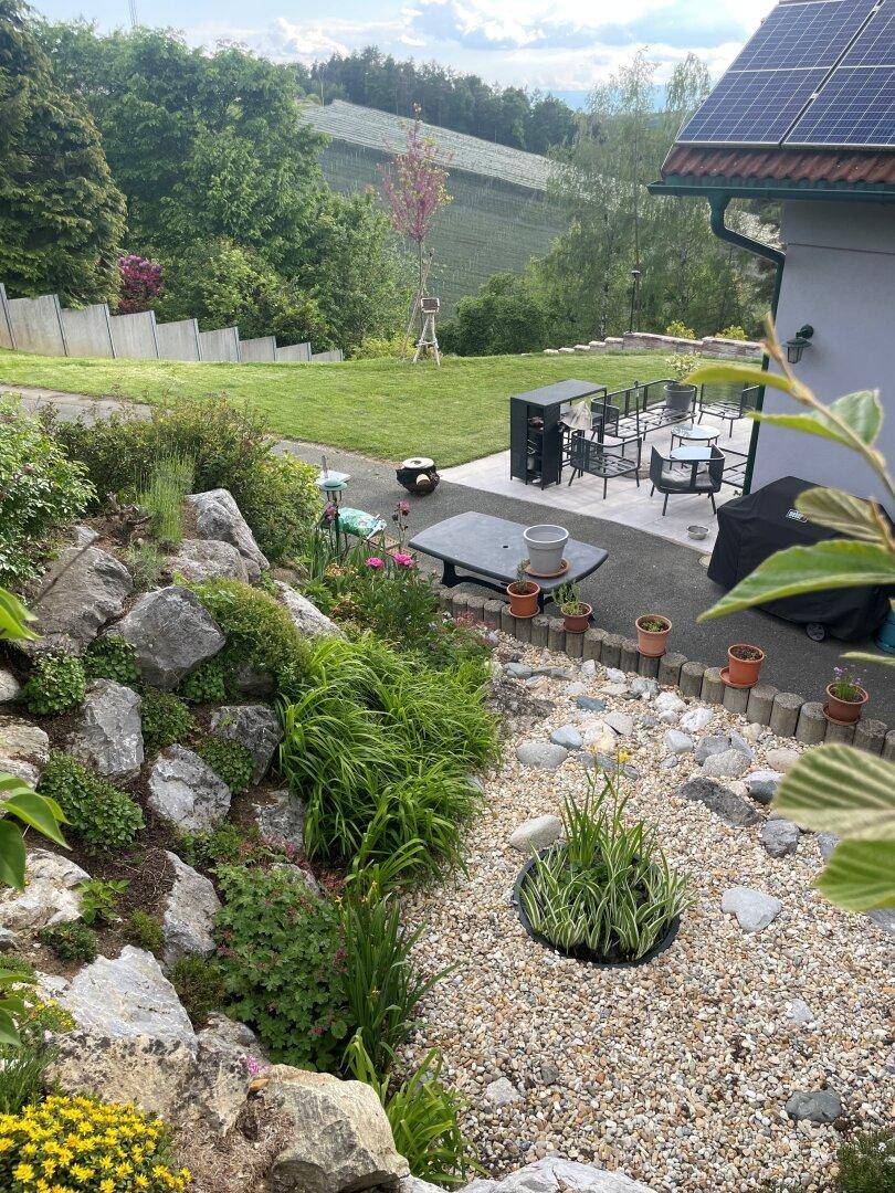 Gepflegter Steingarten mit Kieswegen und Blick auf die Terrasse und die umliegende grüne Landschaft.