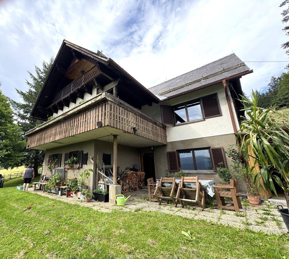 Traditionelles Haus im alpinen Stil mit Holzbalkonen und umgebender Natur unter bewölktem Himmel.