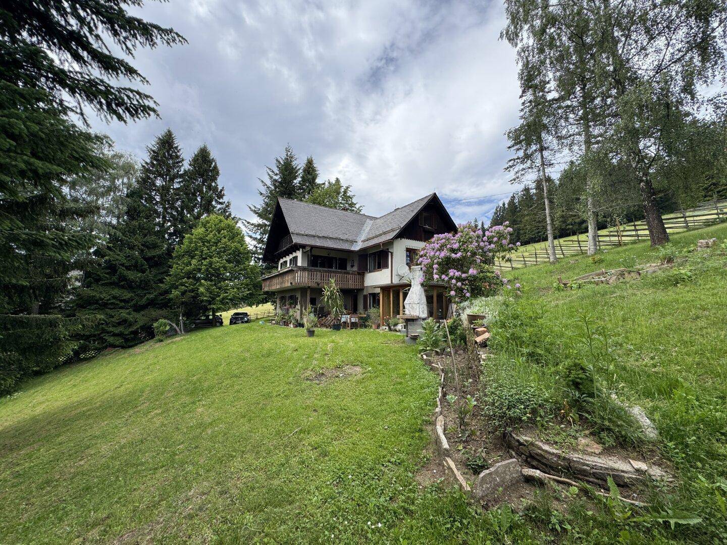 Charmantes Landhaus in idyllischer Hügellandschaft, umgeben von Bäumen und blühenden Sträuchern.