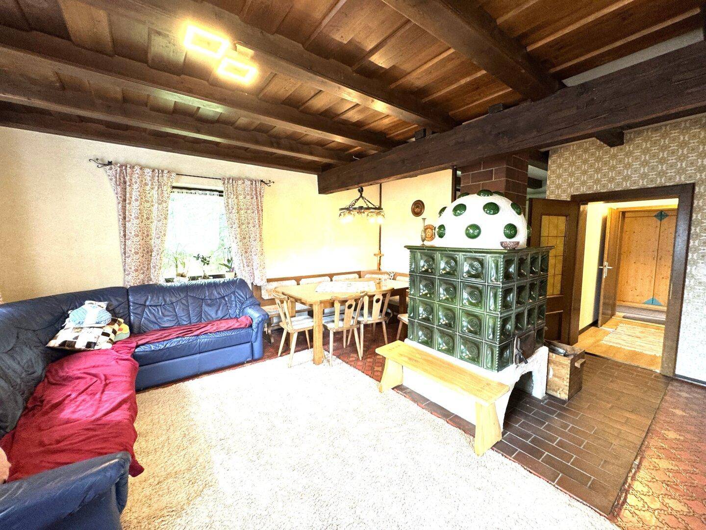 Gemütlicher Wohn-Essbereich mit grünem Kachelofen, Ledersofa und Holzbalkendecke.