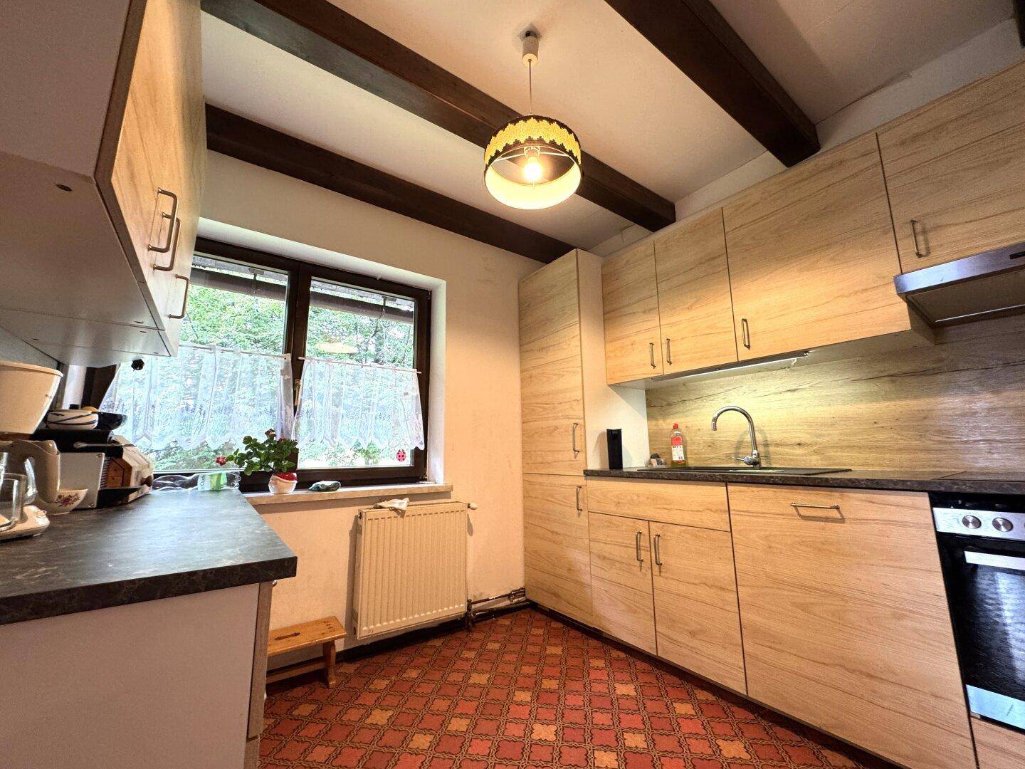 Funktionale Küche mit hellen Holzschränken, Fenster und gemustertem Fliesenboden.