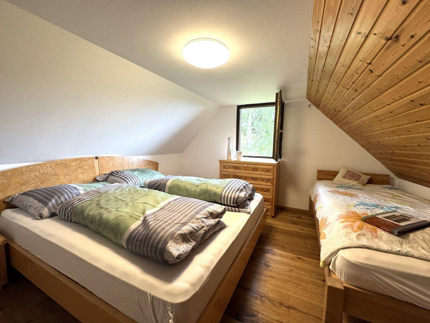 Dachgeschoss-Schlafzimmer mit Doppelbett, Holzboden und schräger Decke, hell und gemütlich.