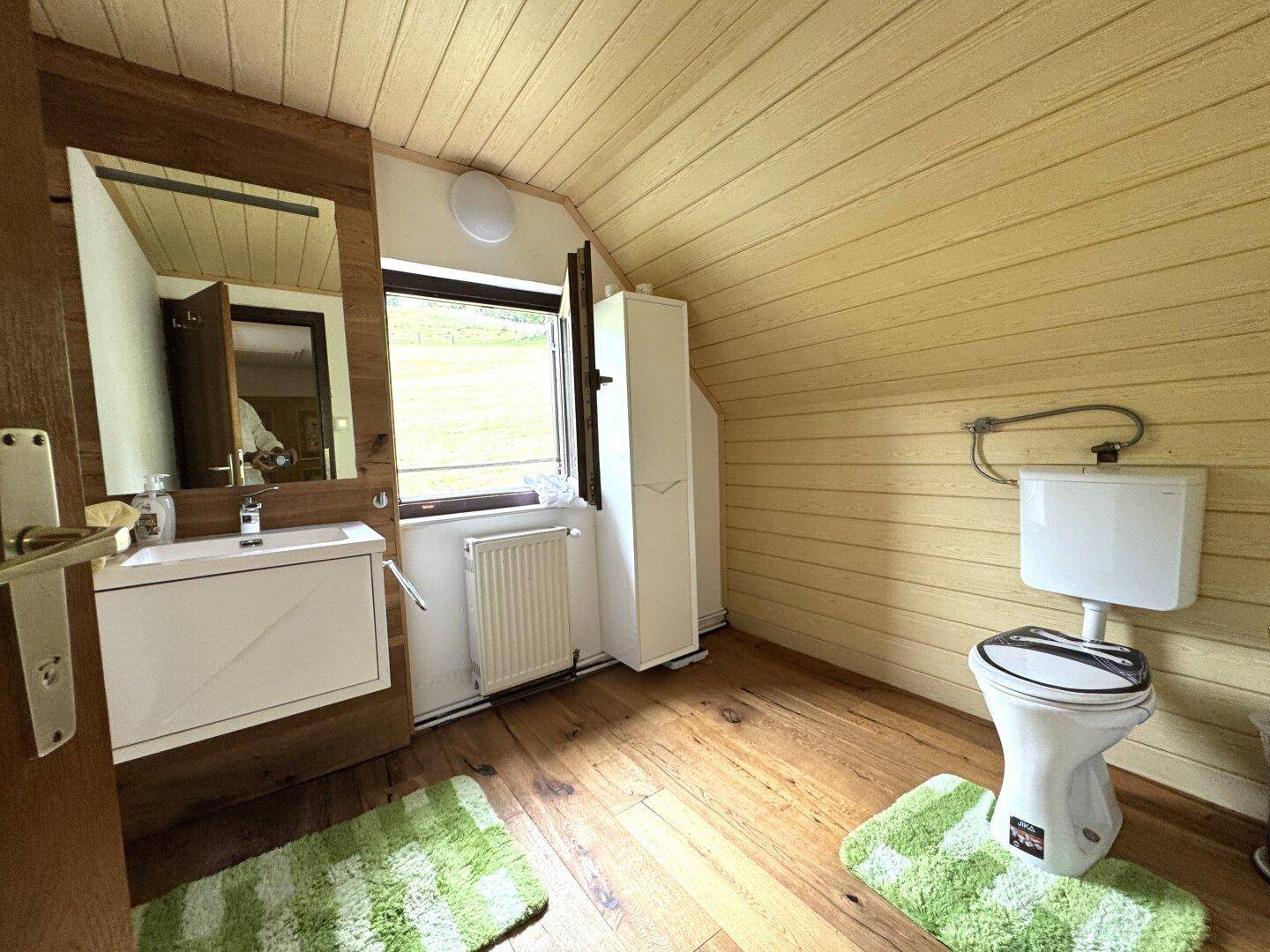 Badezimmer im Dachgeschoss mit schräger Holzdecke, WC, Waschtisch und Fenster.