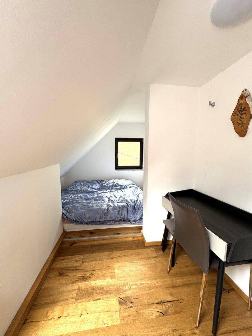 Kleiner Schlafbereich im Dachgeschoss mit Bett, Schreibtisch und Holzboden.