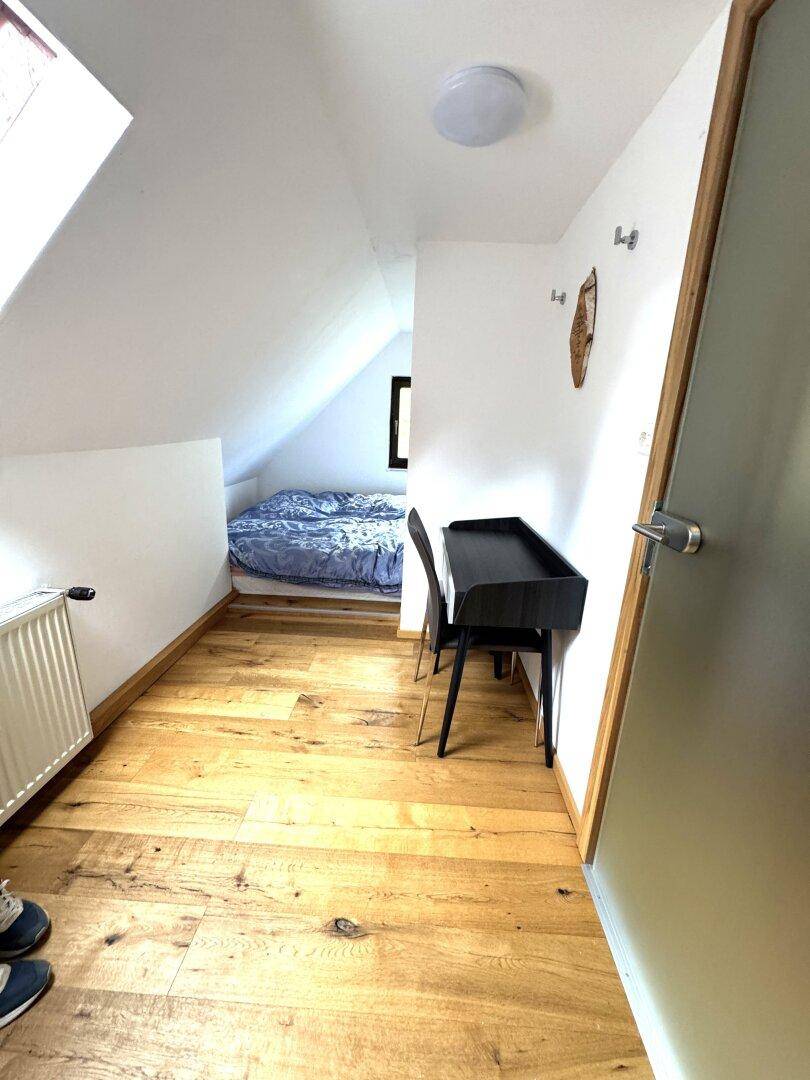 Dachgeschosszimmer mit Schreibtisch und Schlafbereich in einer Nische, mit Holzboden.