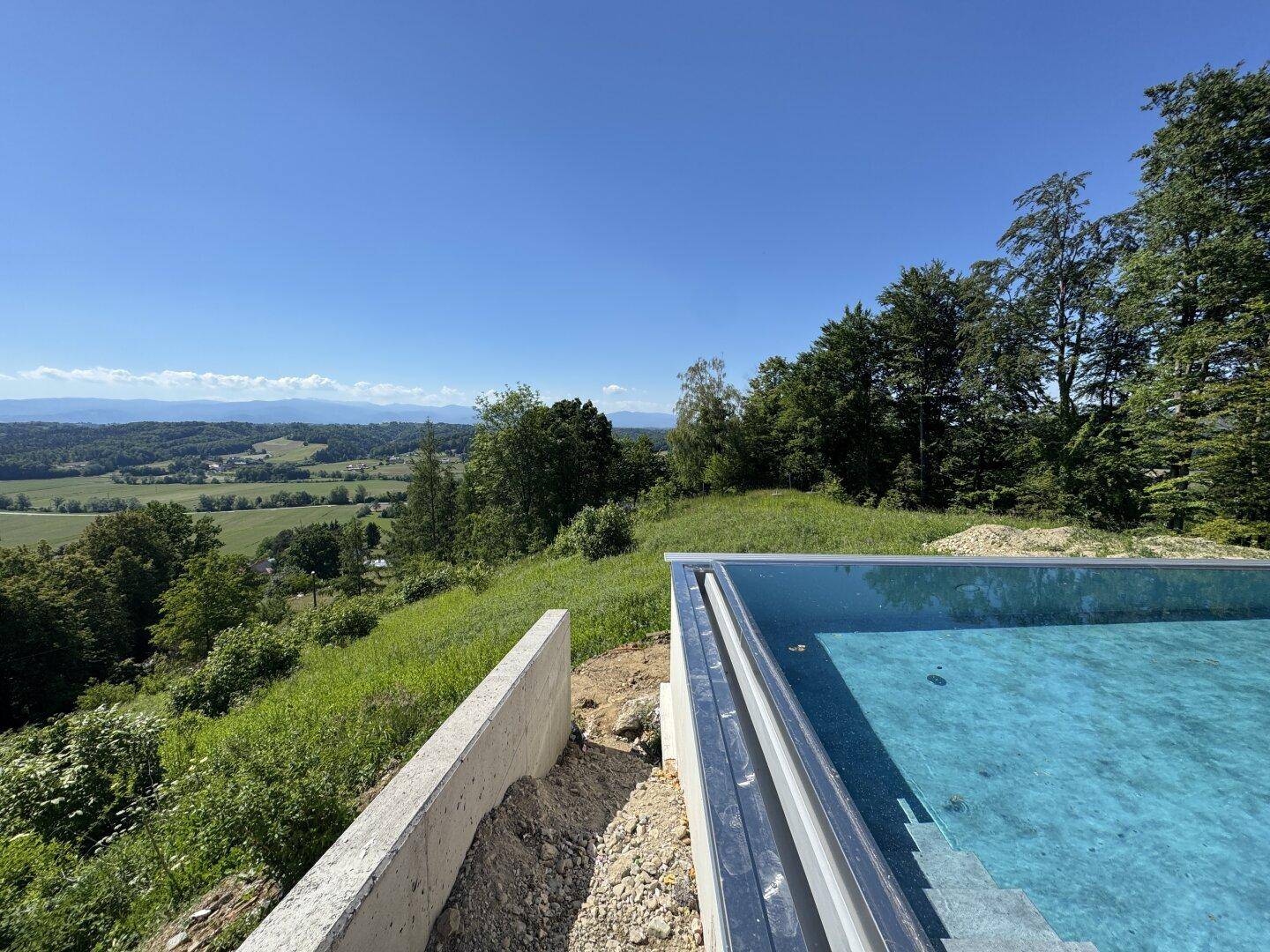 Infinity-Pool am Hang mit atemberaubendem Blick auf die weite grüne Landschaft und Berge.