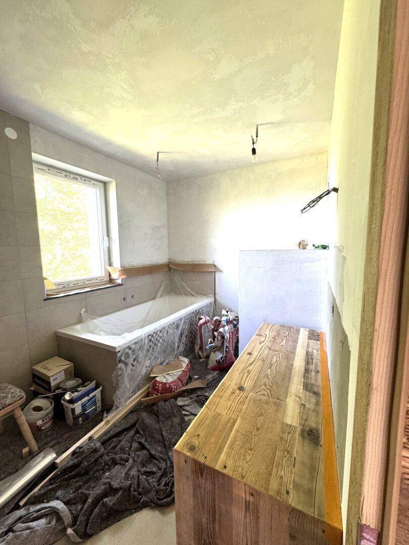Badezimmer im Bau mit Badewanne, Fenster und Holzmöbeln, bereit für die Fertigstellung.