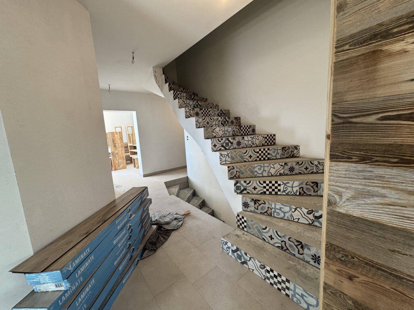 Treppenhaus mit gemusterten Fliesen auf den Stufen und Holzwänden, noch im Bau.