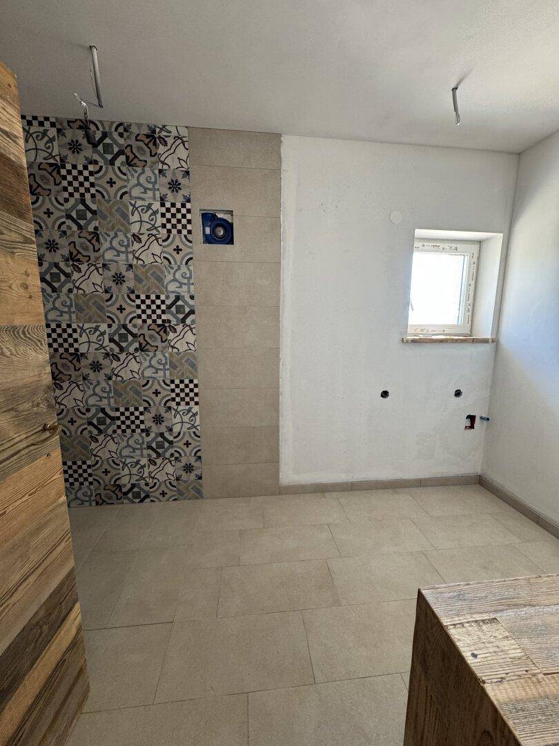 Badezimmer im Bau mit gemusterten Fliesen im Duschbereich und Fenster.