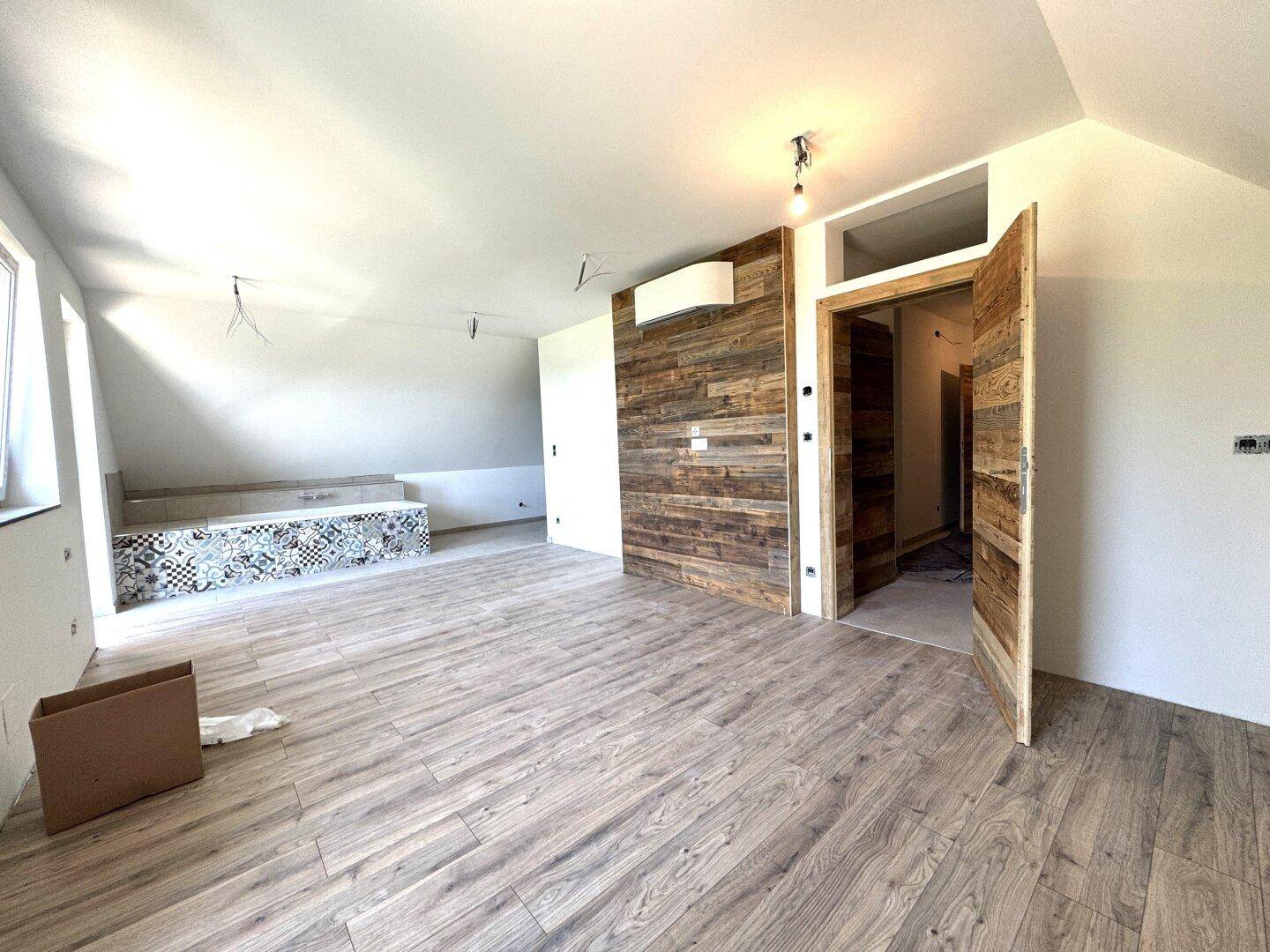 Geräumiger Raum im Dachgeschoss mit Laminatboden, Holzwand und vorbereiteter Badewanne.