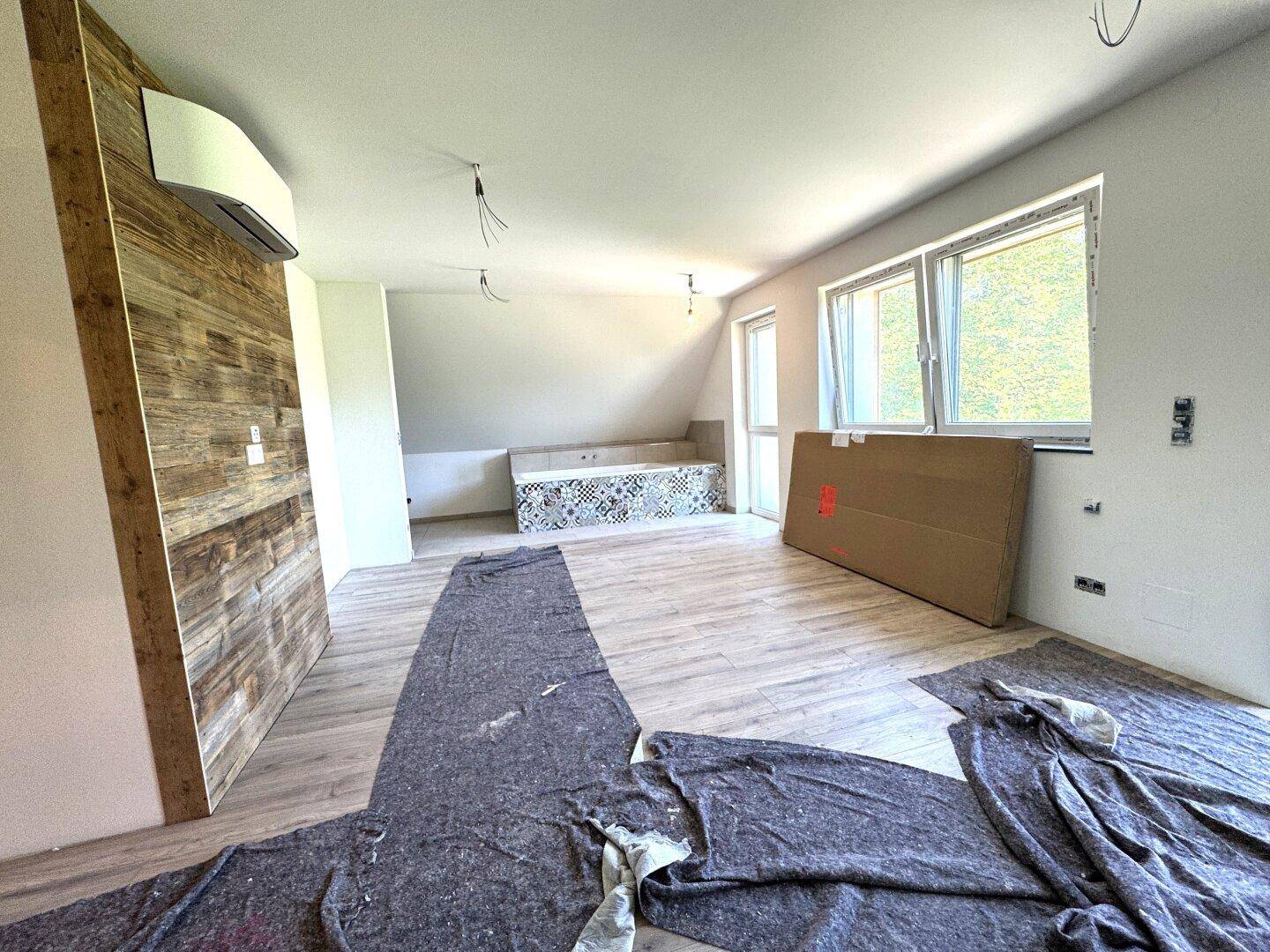 Geräumiger Raum im Dachgeschoss mit Laminatboden, Holzwand und vorbereiteter Badewanne.