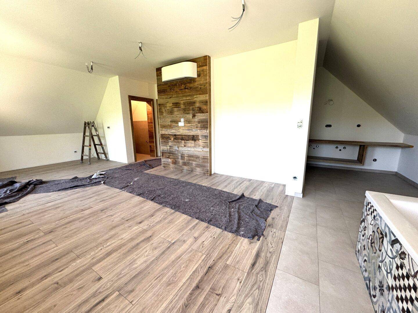 Heller Raum im Dachgeschoss mit Laminatboden, Holzwand und Ablageflächen.