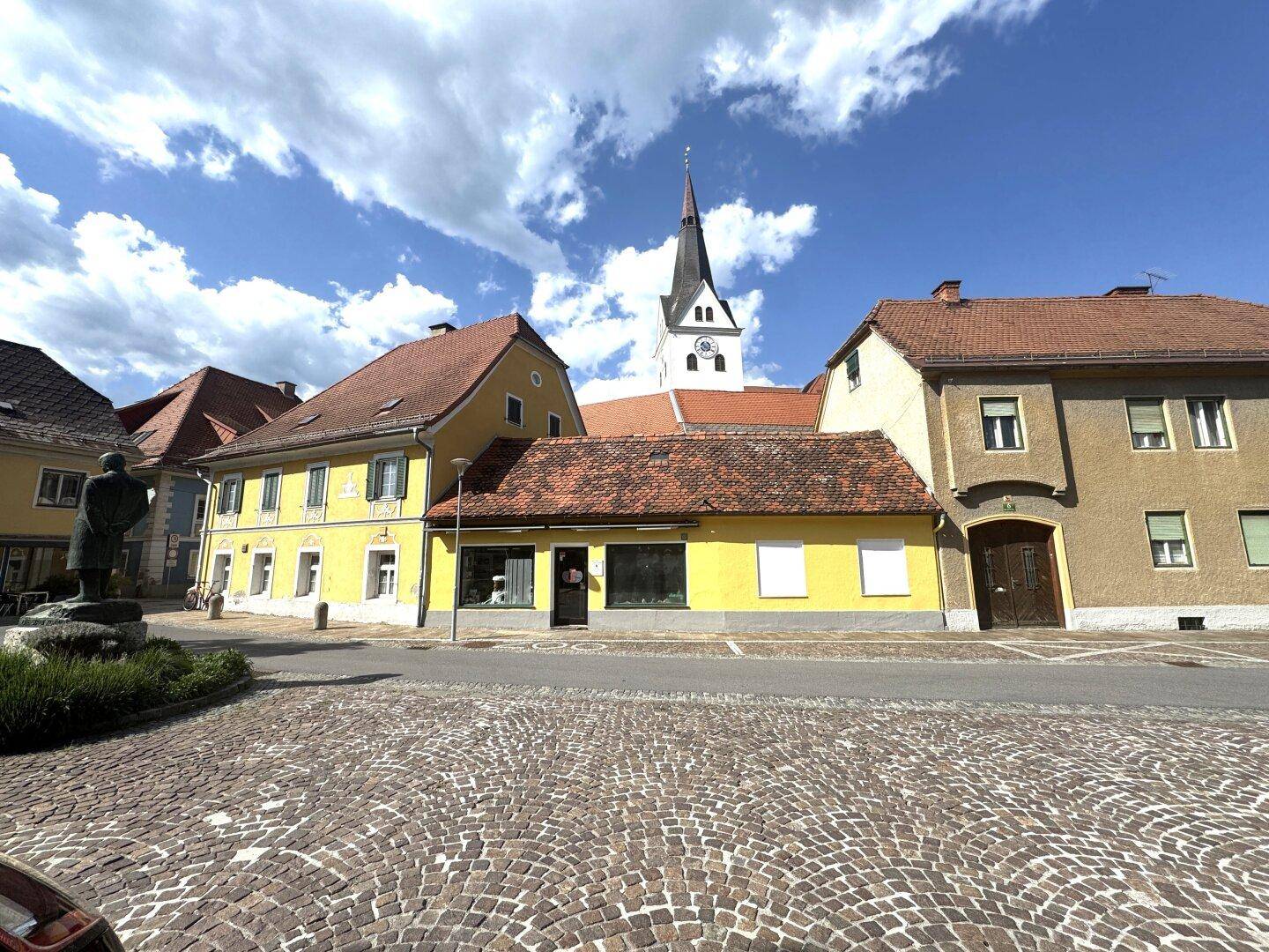 Historische Gebäudezeile mit gelben Fassaden und Kopfsteinpflasterstraße, Kirche im Hintergrund.
