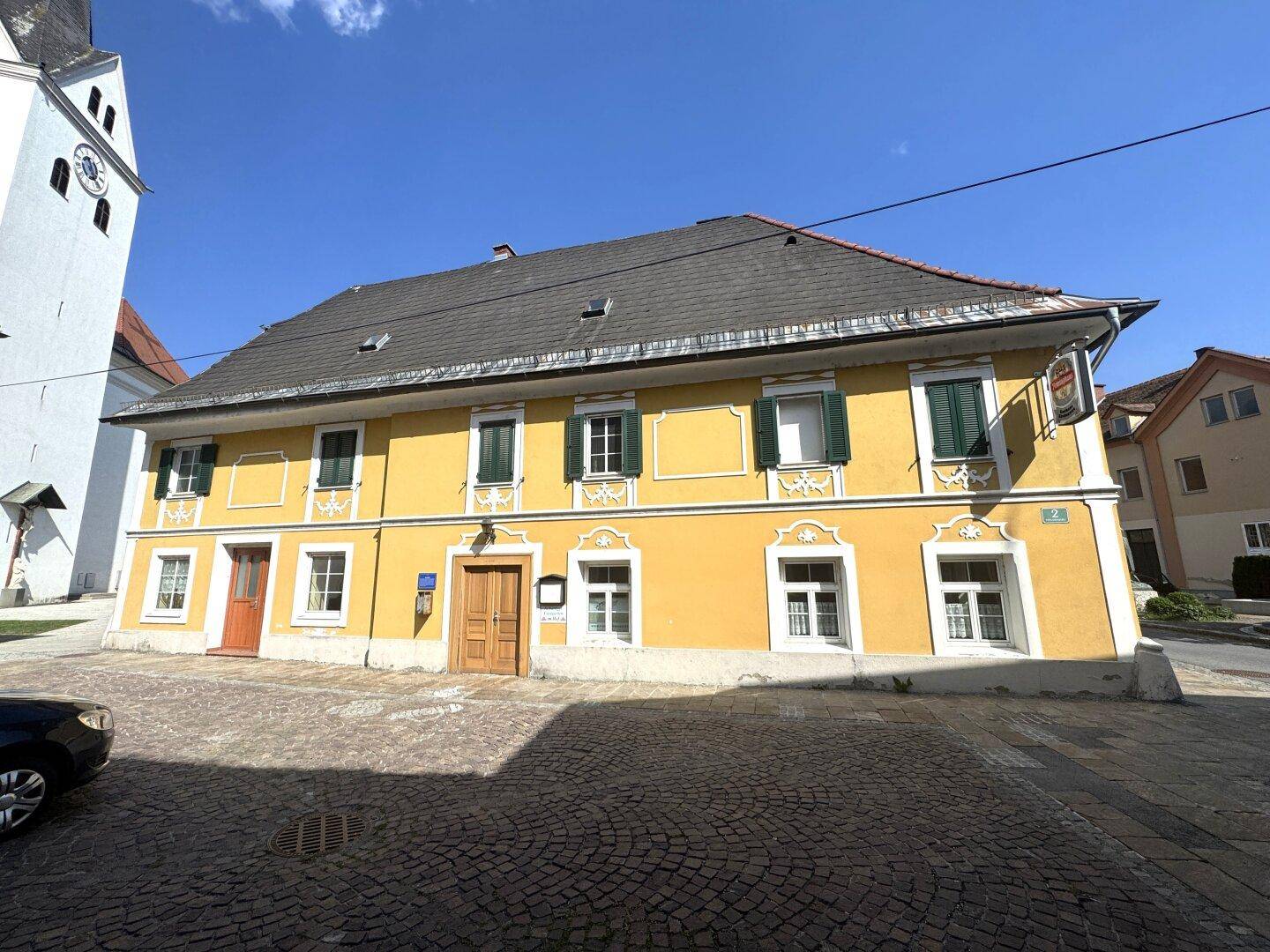 Gelbe historische Fassade mit grünen Fensterläden und Holztüren unter klarem Himmel.