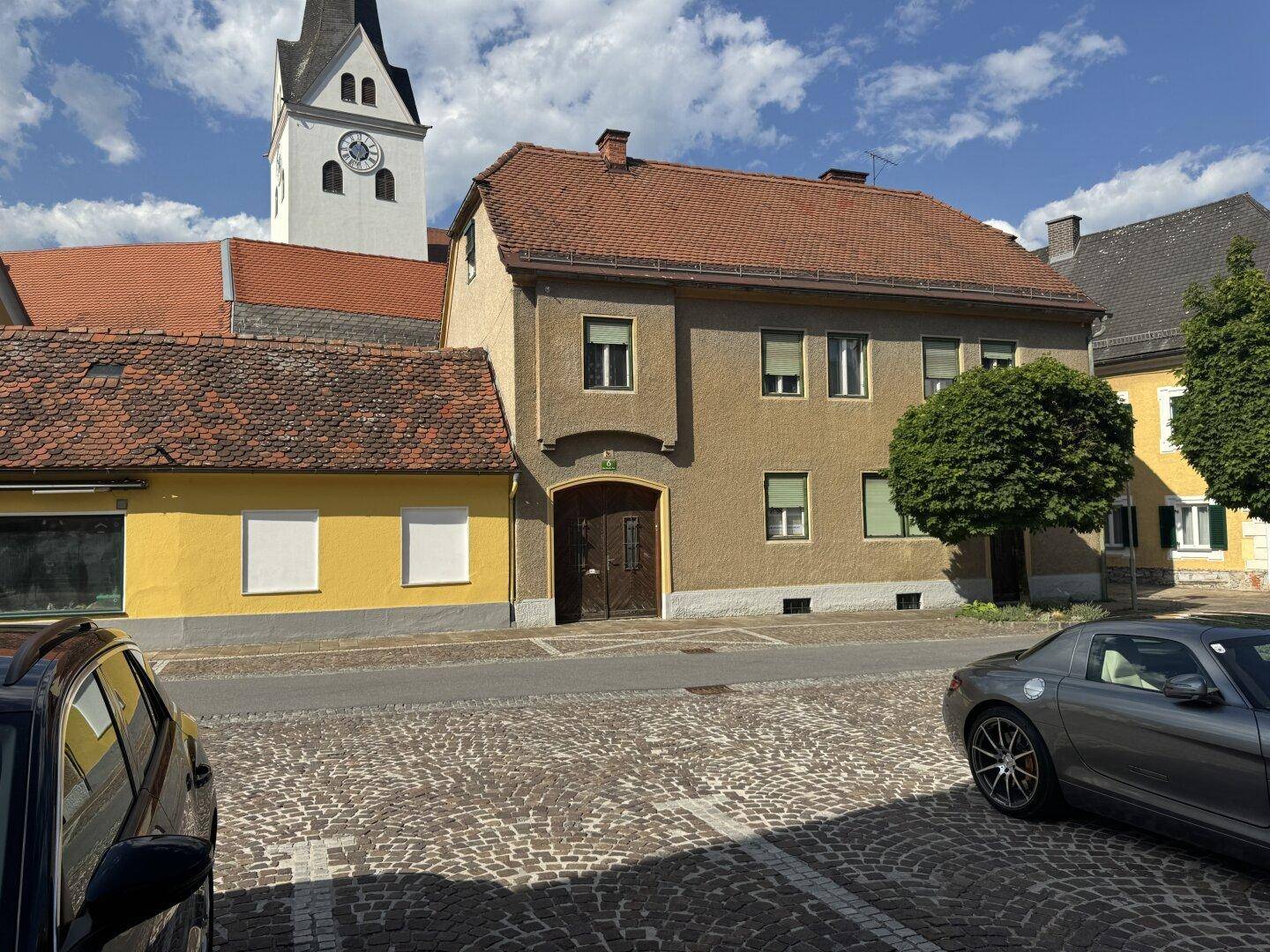 Historisches Gebäude mit brauner Fassade und geparkten Autos auf Kopfsteinpflasterstraße.