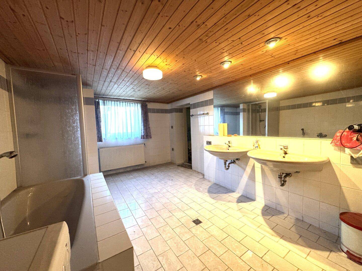 Geräumiges Badezimmer mit zwei Waschbecken, Badewanne und Holzdecke, gefliestem Boden.