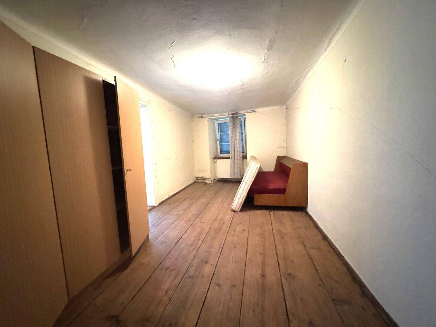 Leeres Schlafzimmer mit Holzdielenboden, weißen Wänden und einem Fenster.