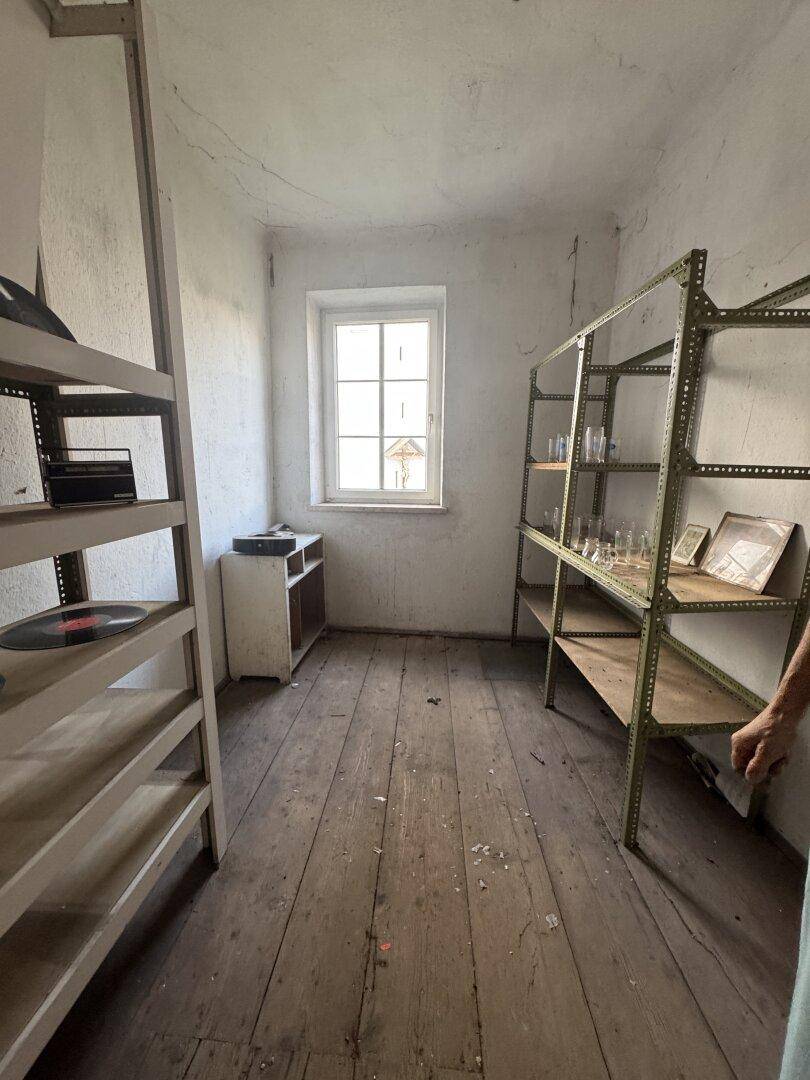 Einfacher Abstellraum mit Holzregalen, Holzdielenboden und einem Fenster.