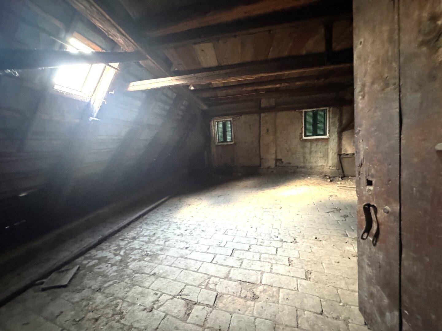 Geräumiger Dachboden mit Holzbalken, Ziegelboden und Dachfenster, viel natürliches Licht.