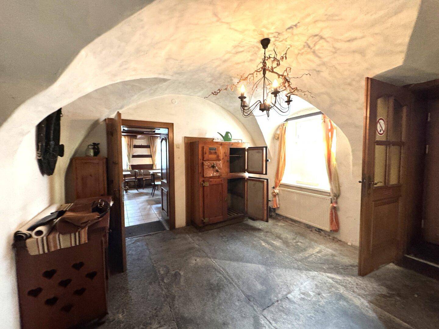 Historischer Eingangsbereich mit Gewölbedecke, Steinfliesenboden und rustikalen Holzmöbeln.