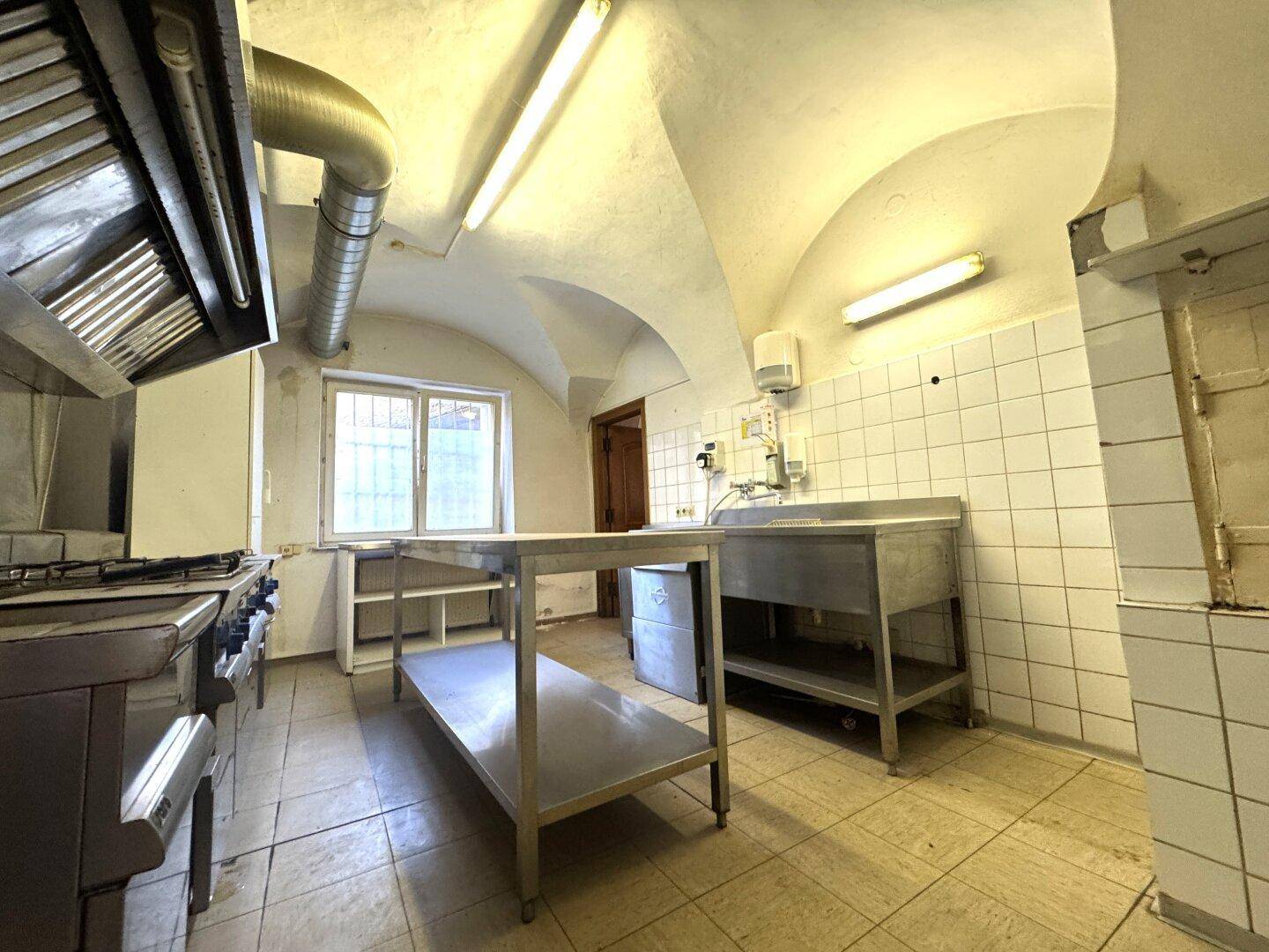 Große Gewerbeküche mit Edelstahlmöbeln, Gasherd und Gewölbedecke, gefliestem Boden.
