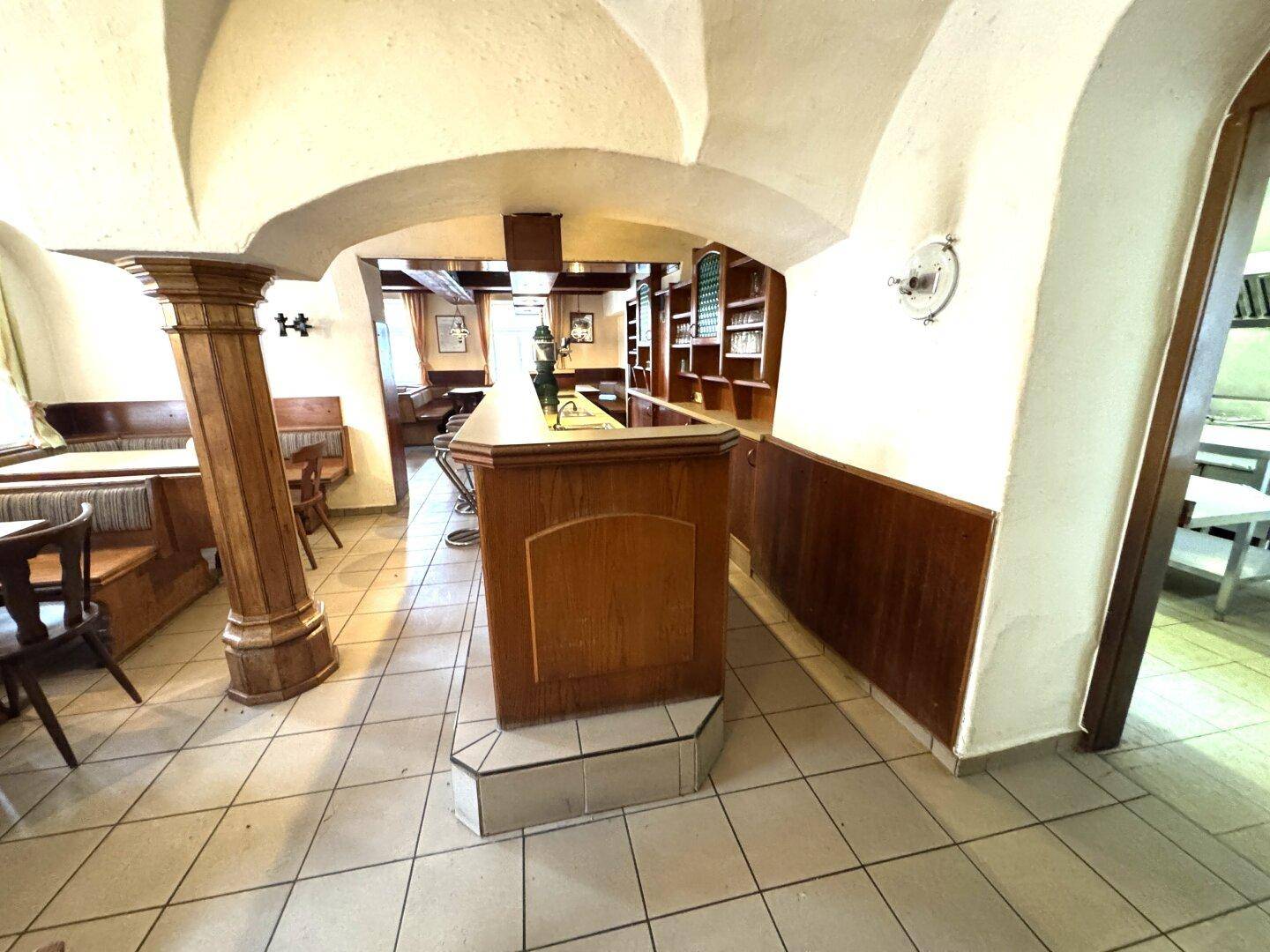 Gastraum mit Gewölbedecke, Holzvertäfelung und Bar, gefliestem Boden.