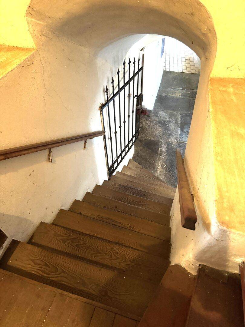 Alte Holztreppe mit schmiedeeisernem Gitter und gewölbtem Durchgang.