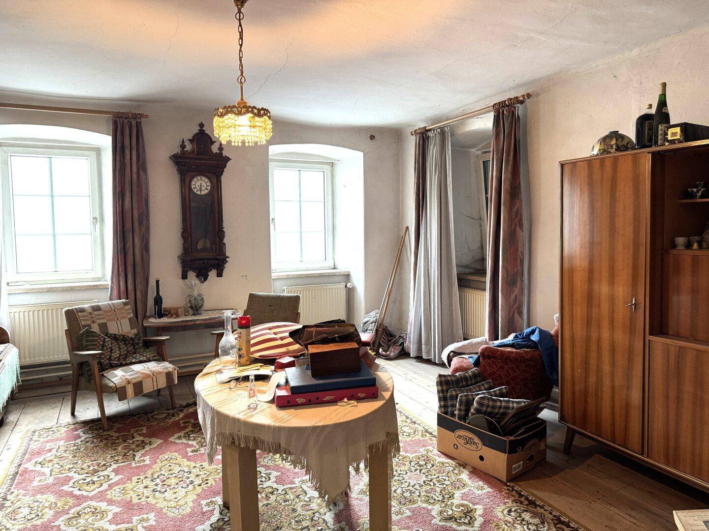 Wohnzimmer im Vintage-Stil mit Teppich, alten Möbeln und zwei Fenstern.