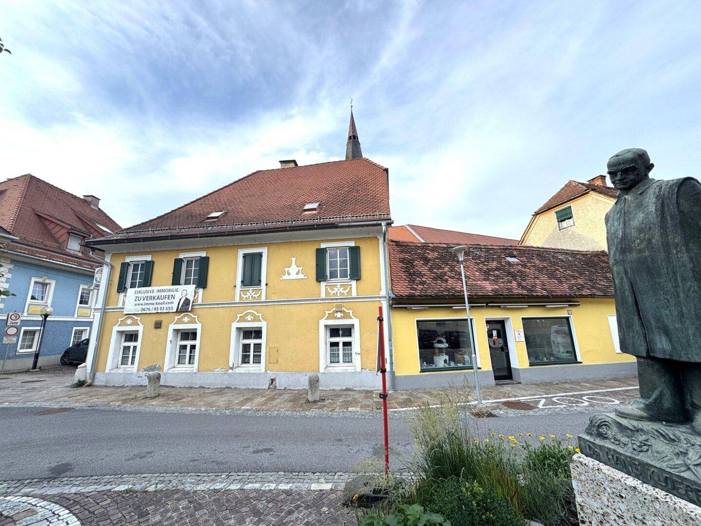 Historisches gelbes Gebäude mit rotem Ziegeldach und einem 'Zu Verkaufen'-Schild an der Fassade.
