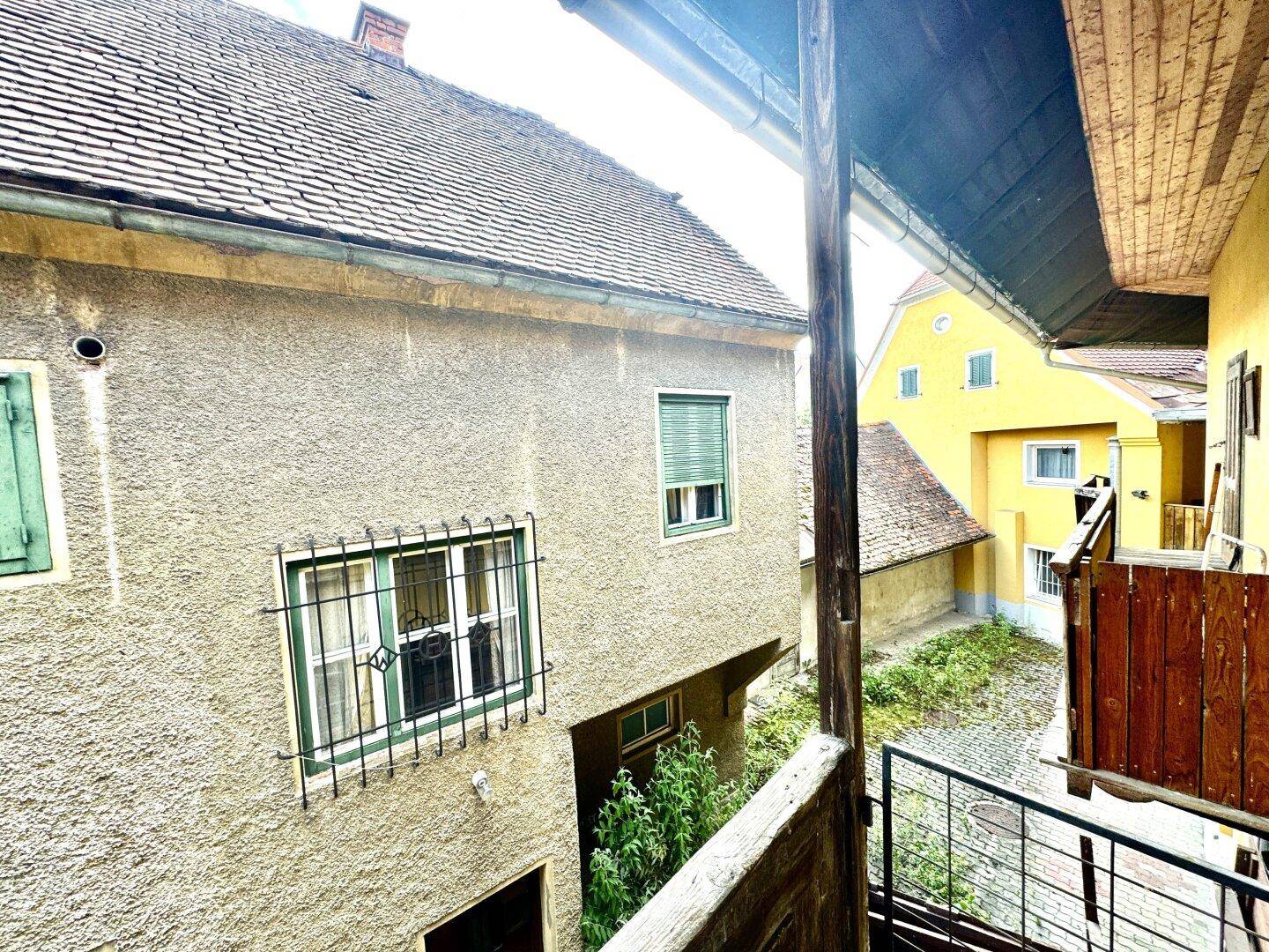 Blick von einem Balkon auf einen Innenhof und angrenzende Gebäude mit traditioneller Architektur.
