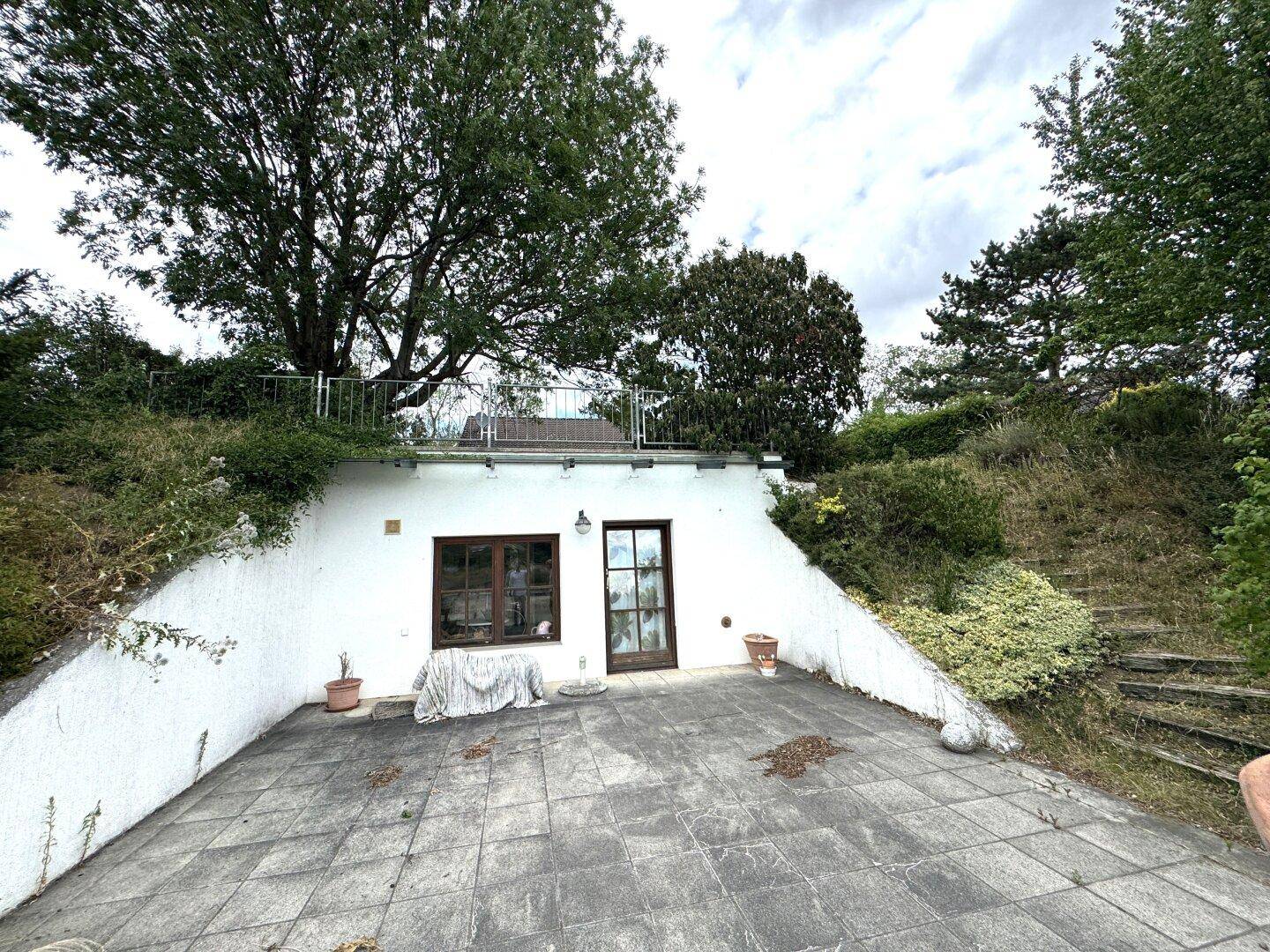 Unterirdischer Eingangsbereich mit gepflasterter Terrasse und Treppe zum oberen Gartenbereich.