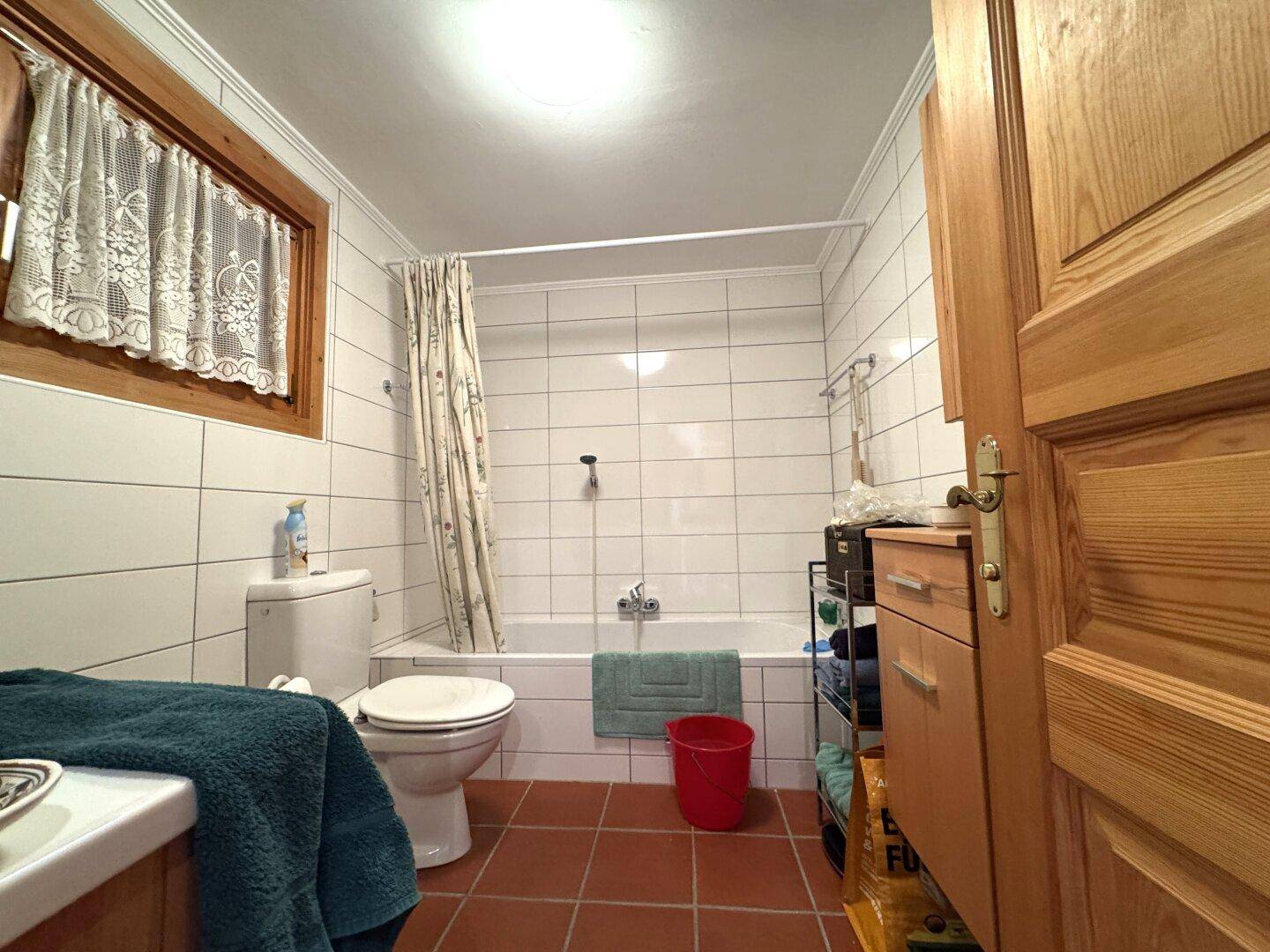 Helles Badezimmer mit weißen Fliesen, Badewanne und Fenster, ausgestattet mit Holzmöbeln.