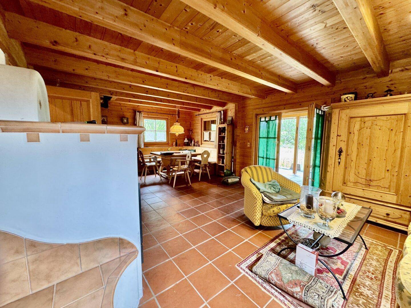 Geräumiger Wohn- und Essbereich mit Holzbalkendecke, Kachelofen und Zugang zur Terrasse.