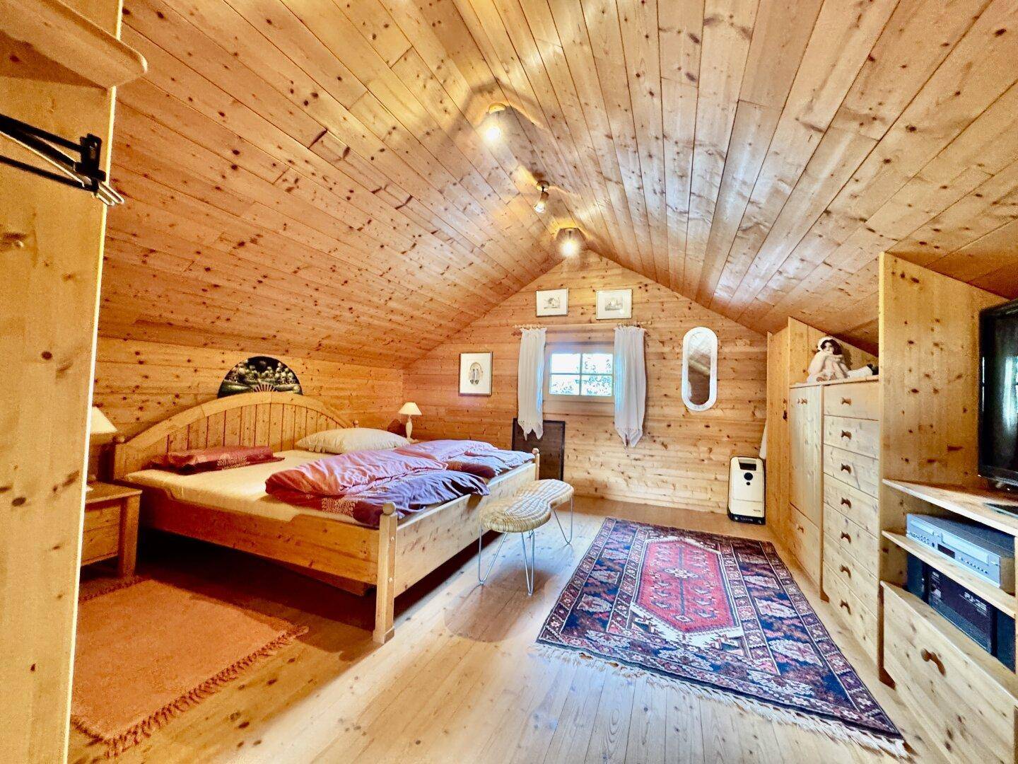 Helles Schlafzimmer im Dachgeschoss mit Holzbett, Dachschräge und traditionellem Teppich.
