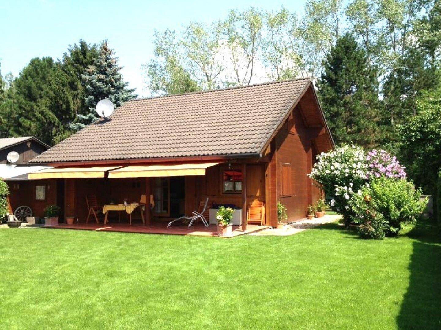 Gemütliches Holzhaus mit großer Rasenfläche und überdachter Terrasse, ideal für entspannte Stunden im Grünen.