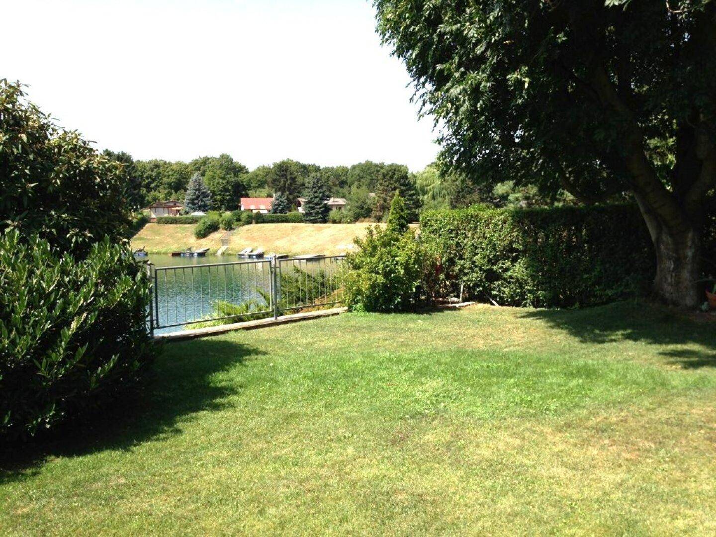 Gepflegter Gartenbereich mit direktem Zugang zu einem See, umgeben von üppiger Vegetation und Bäumen.