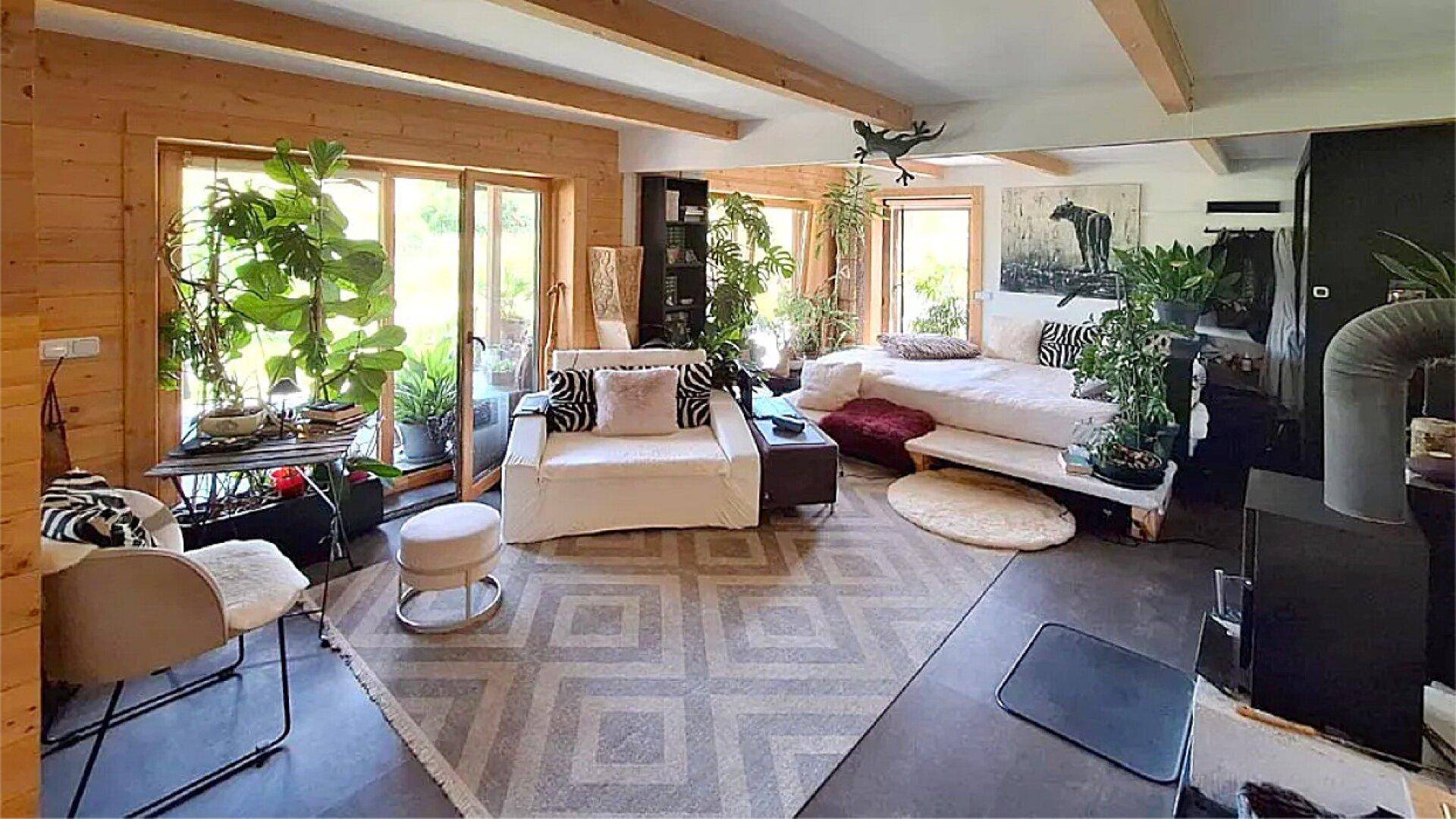 Gemütliches Wohnzimmer mit Holzwänden, sichtbaren Deckenbalken und vielen Zimmerpflanzen.
