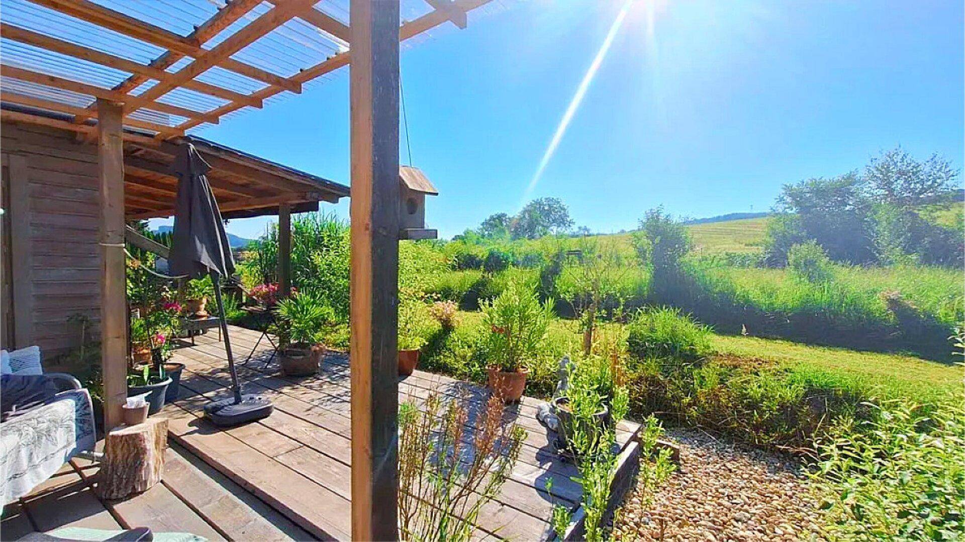 Sonnige Holzterrasse mit Blick auf die weite grüne Landschaft unter strahlend blauem Himmel.