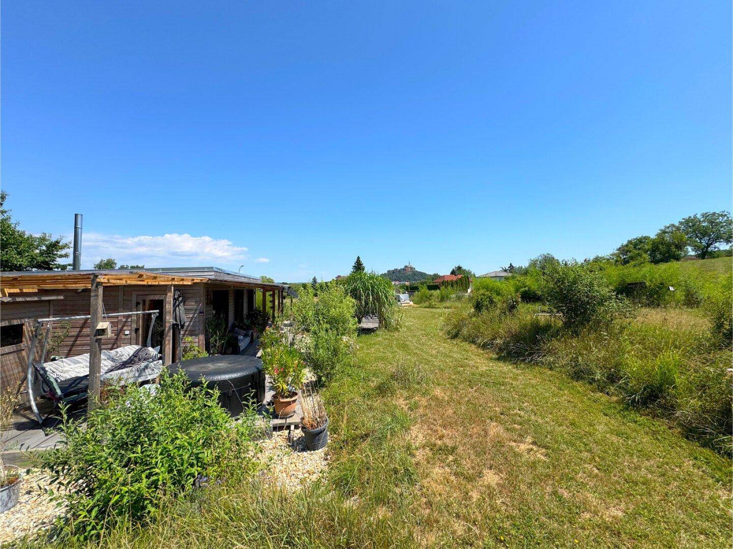 Weitläufiger Gartenbereich mit Holzhaus, Whirlpool und viel Grünfläche unter blauem Himmel.
