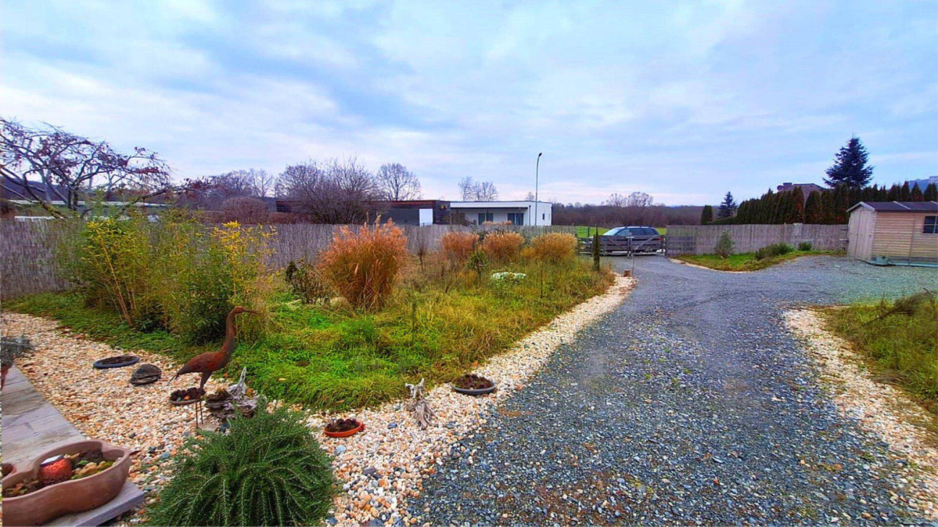Kiesauffahrt und Gartenbereich mit herbstlicher Bepflanzung unter einem bewölkten Himmel.