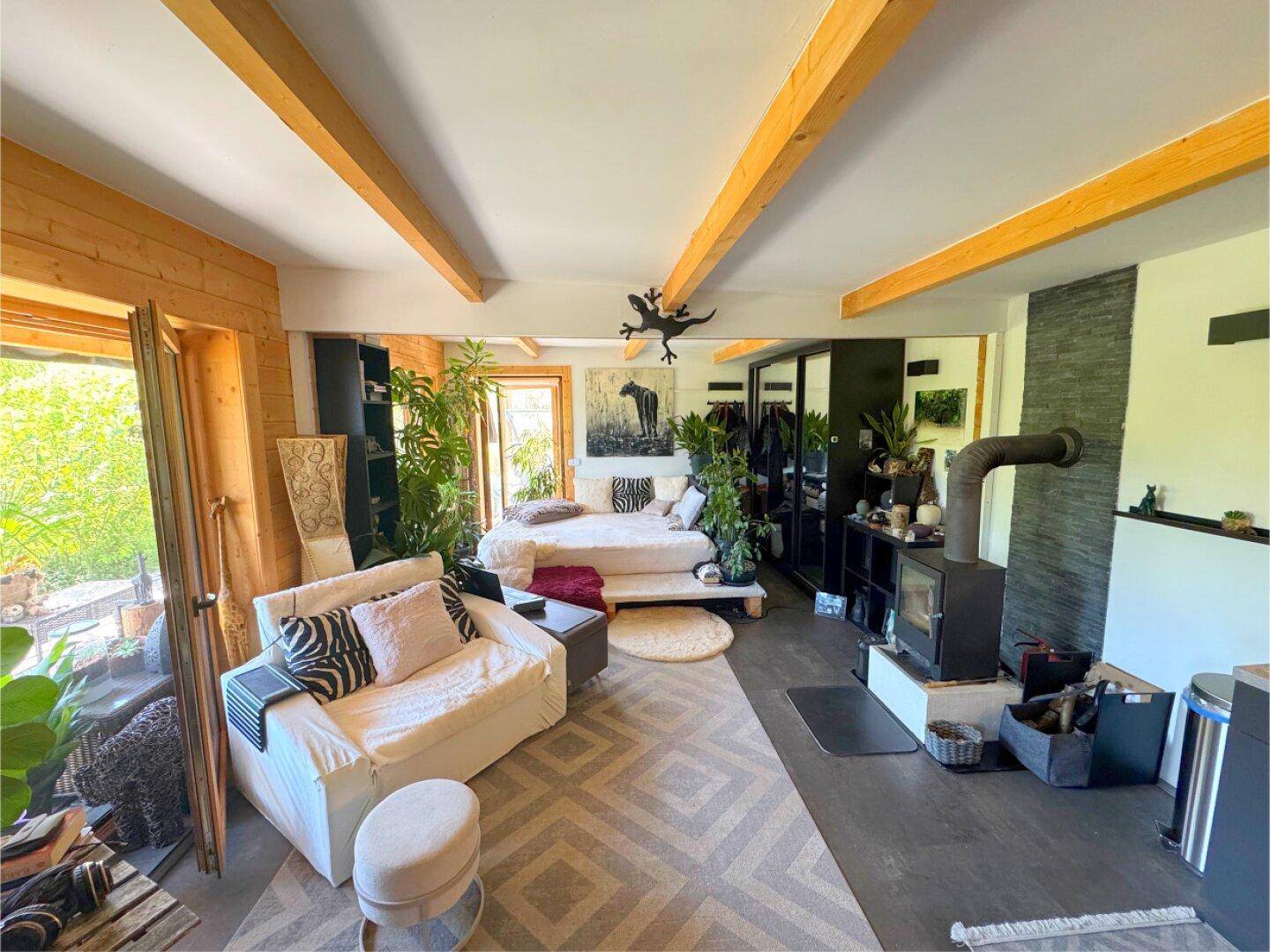 Helles Wohnzimmer mit Holzwänden, Kaminofen und modernen Möbeln, umgeben von Pflanzen.