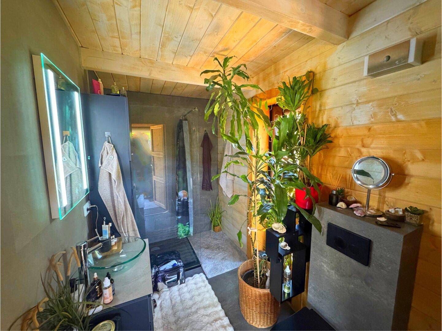 Modernes Badezimmer mit Holzwänden, Glaswaschbecken und großer Dusche, dekoriert mit Pflanzen.