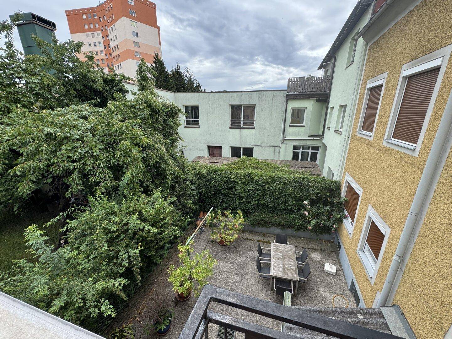 Blick von oben auf den grünen Innenhof mit Sitzbereich und hohen Bäumen.