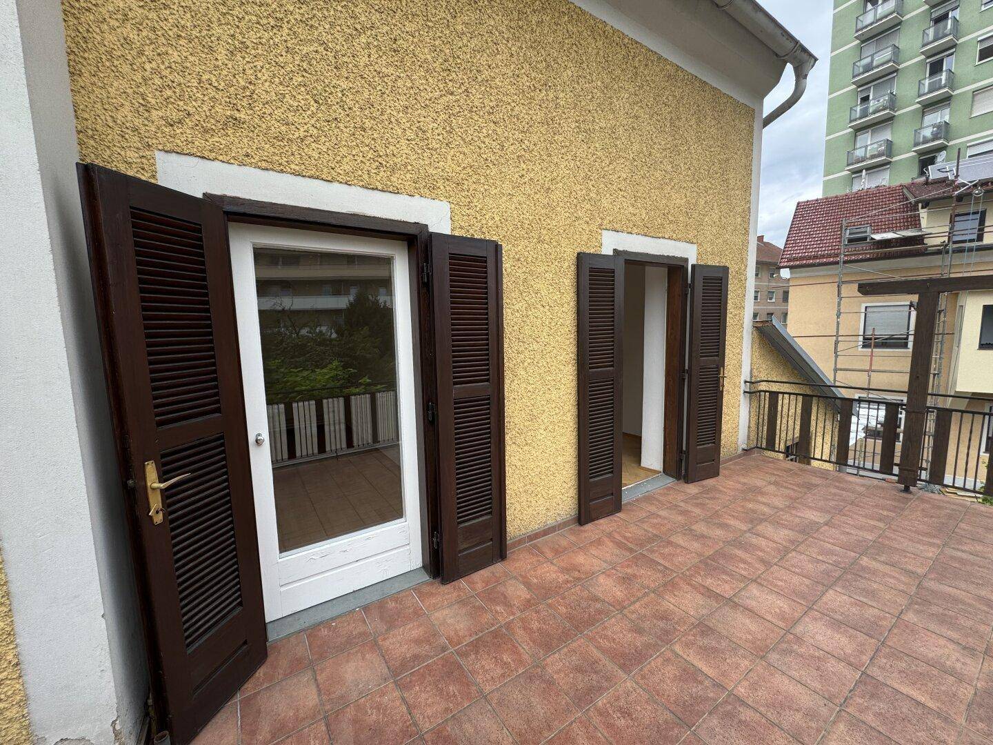 Große geflieste Terrasse mit braunen Fensterläden und Blick auf die Umgebung.