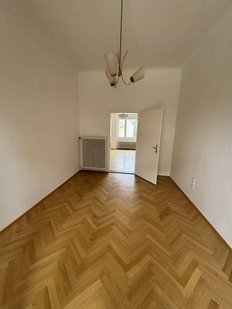 Helles Zimmer mit Fischgrätparkett und einfacher Deckenleuchte, bereit zur Einrichtung.
