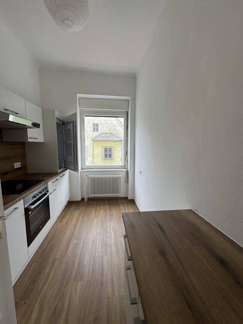 Moderne Küche mit weißen Schränken, Holzarbeitsplatte und Fensterblick.