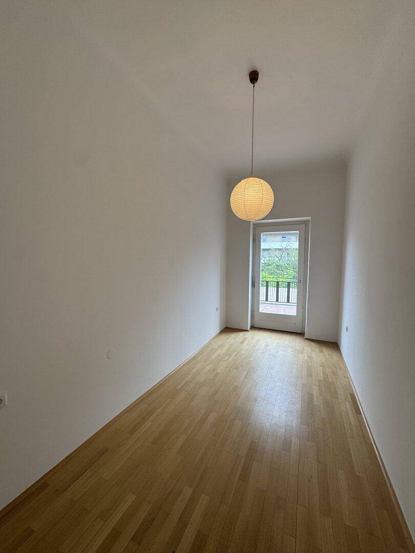 Schmaler Raum mit Holzboden, Papierlampe und Zugang zu einem kleinen Balkon.